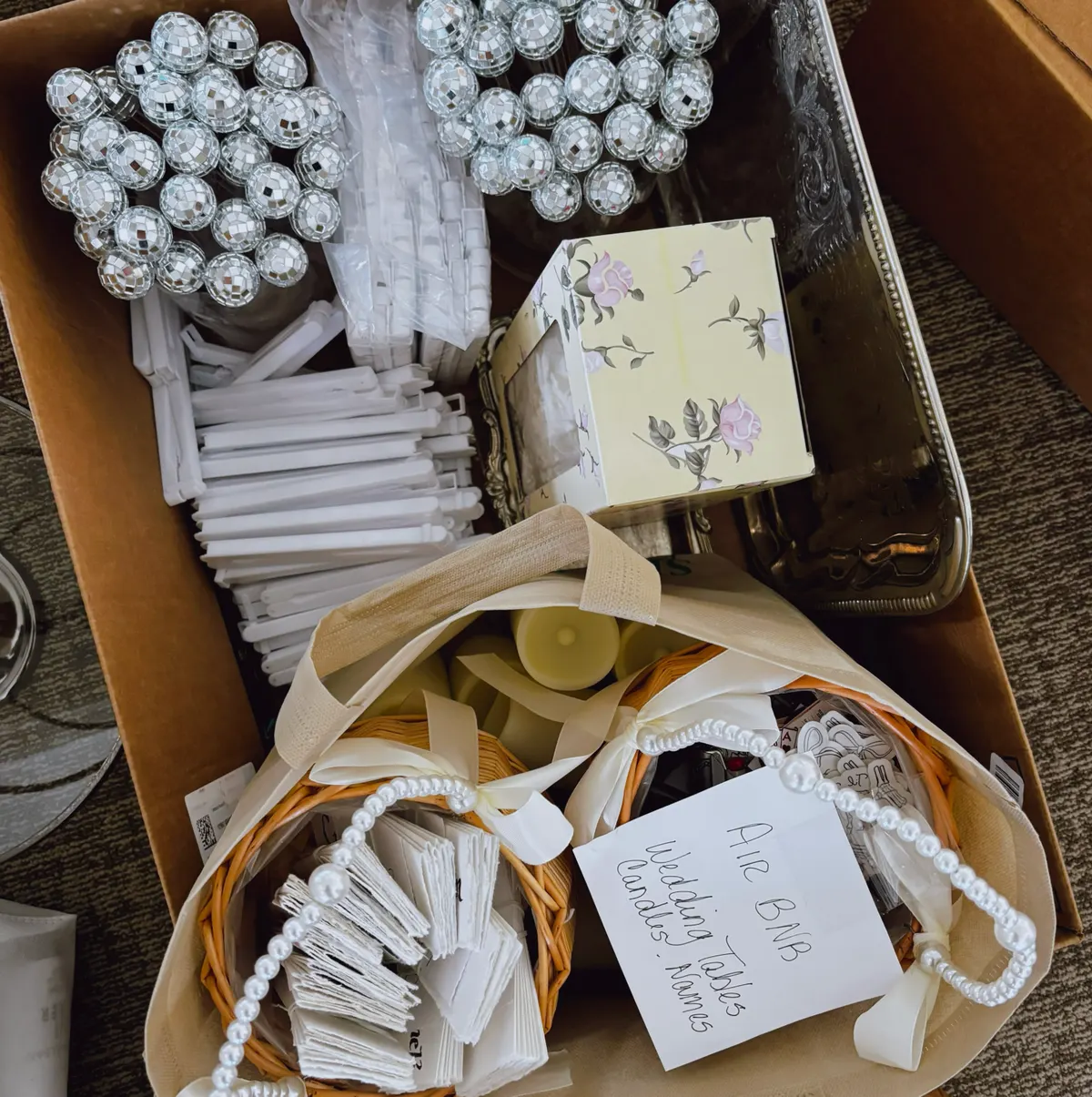 A packed box of wedding supplies: disco-ball favors, place cards and pearl-trimmed baskets