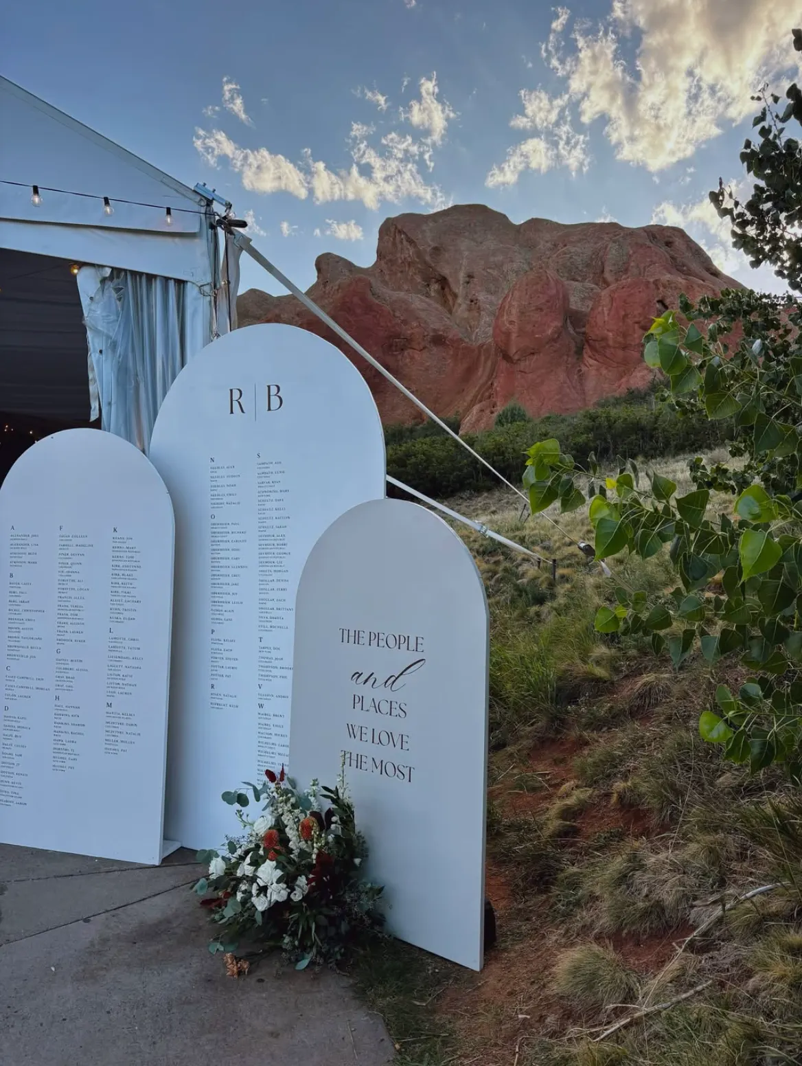 Arched seating-chart signs and flowers outside a wedding tent below Colorado red rocks